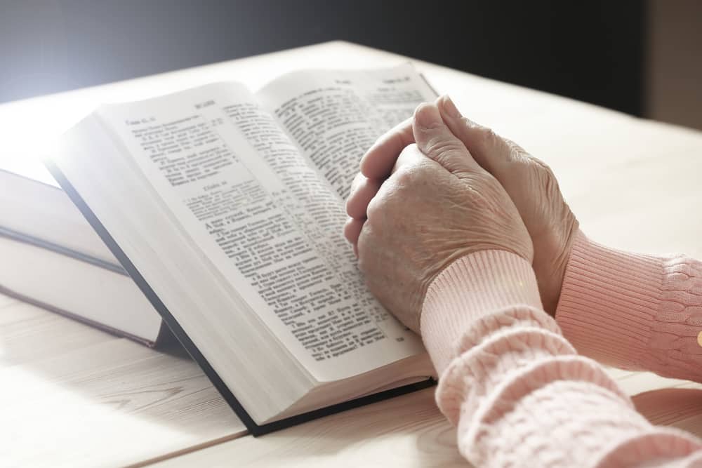 Senior hands clasped on top of open bible