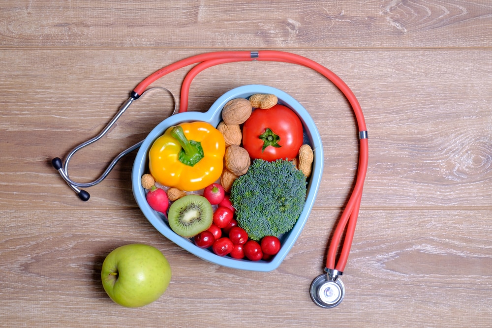 Healthy food in heart-shaped container on wood surface with stethoscope