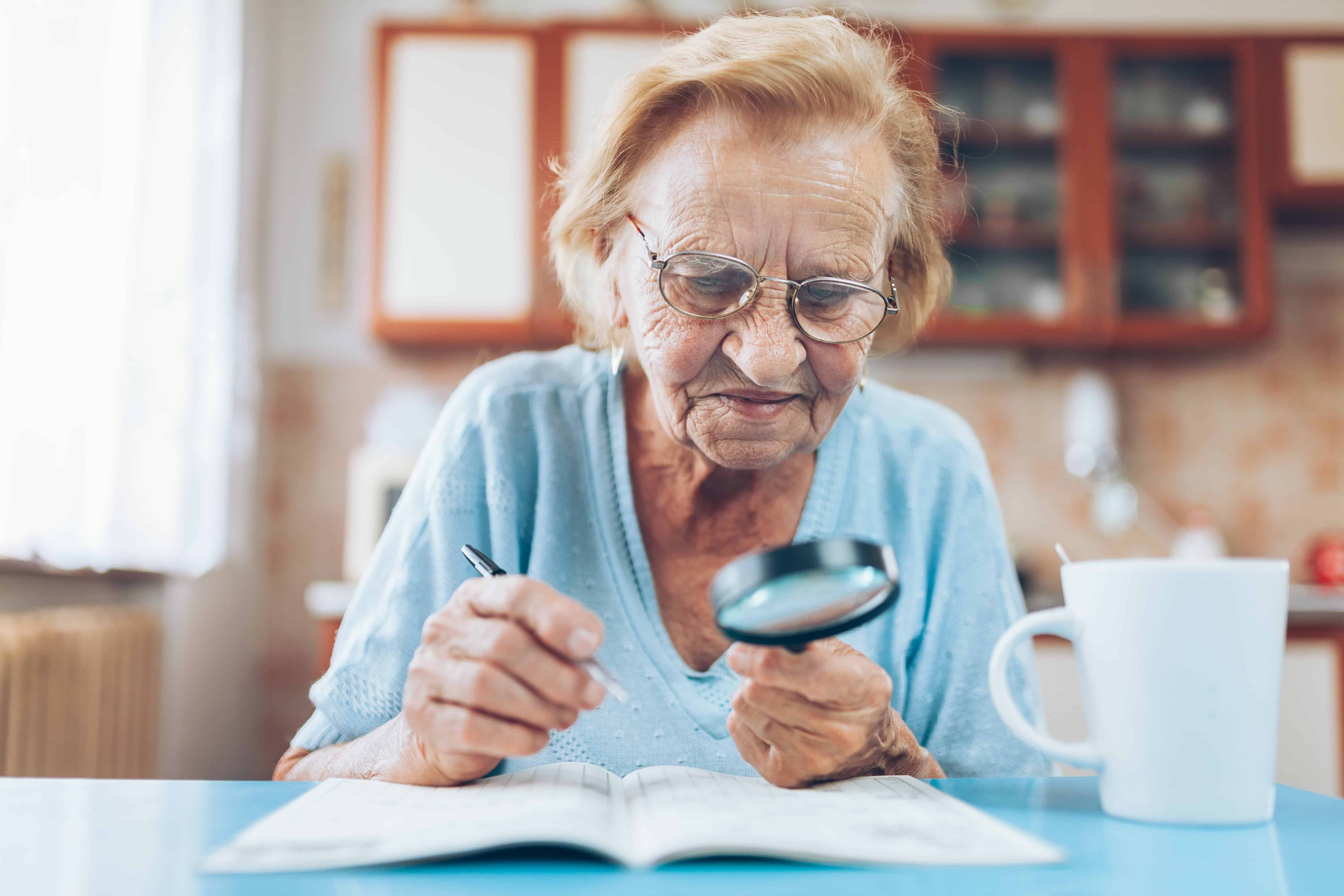 senior woman using magnifying glass to play sudoku in activity book